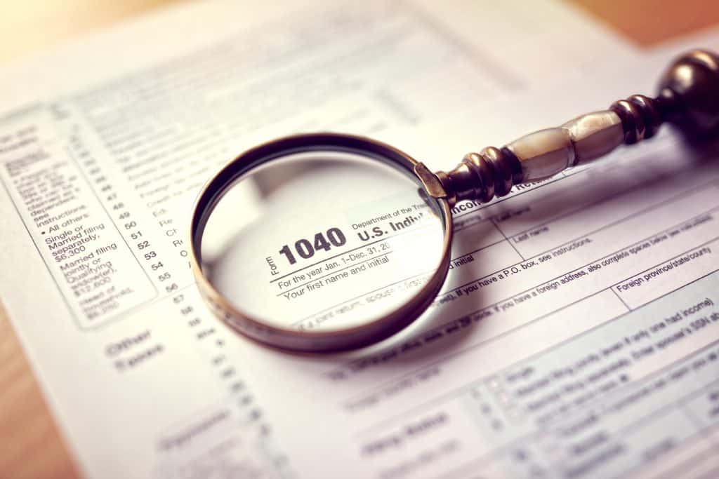 Looking at a 1040 2016 individual tax return form with a magnifying glass, because when filling out a 1040 2016 by hand instead of electronically, you're more likely to make mistakes.